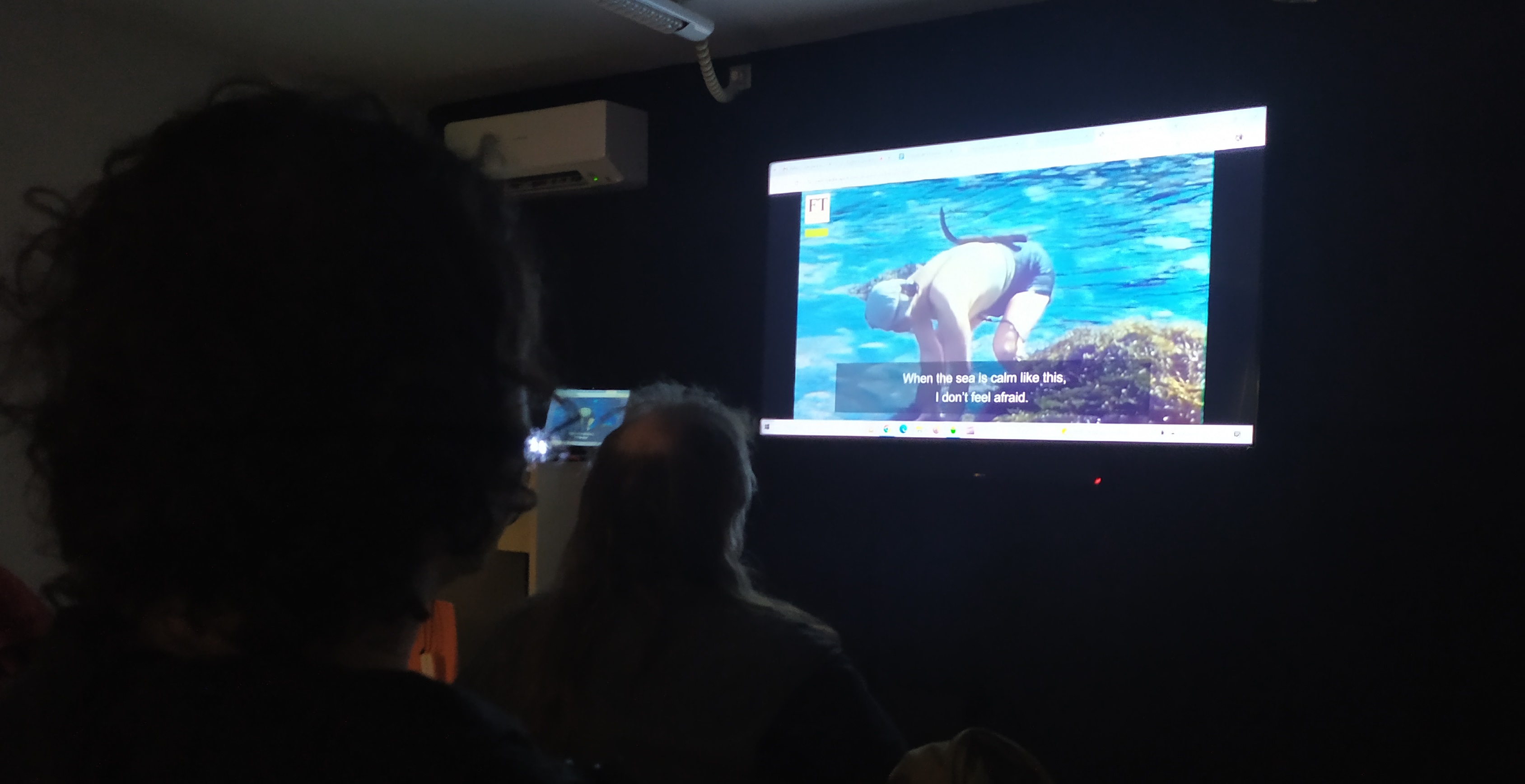 Interior de Sala de Audiovisiales del Centro Cívico Tomasa Cuevas, se ve a personas mirando el video sobre las Haenyeo